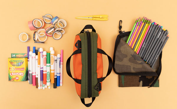 Texturized Orange Grab Bag surrounded by school supplies and an A5 size Ghost Whale Pouch in Beaver Camo.